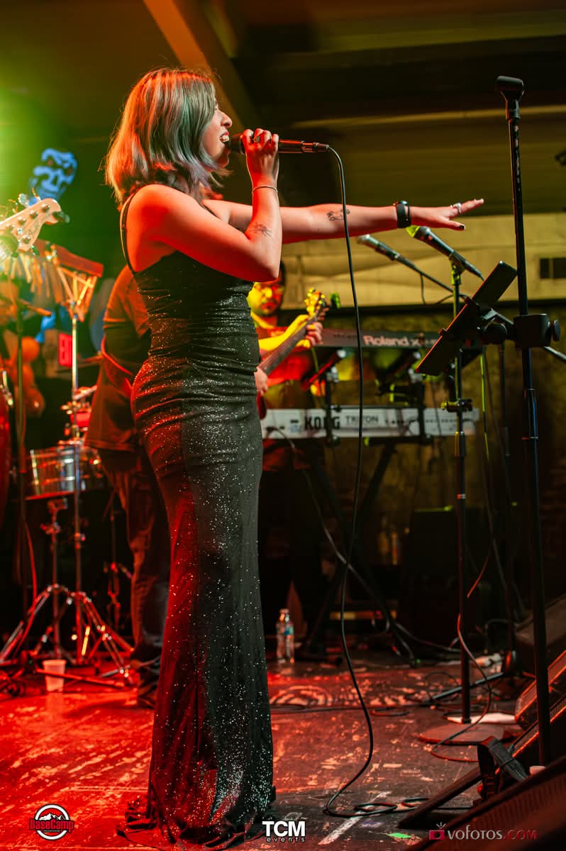 Female vocalist in a sparkling gown reaching toward the audience